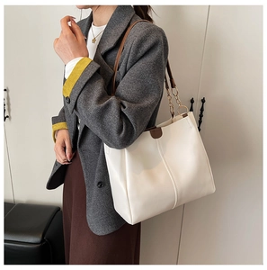 Detail of white leather tote bag featuring gold chain ring and brown shoulder strap accessory