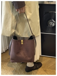 Détail d'un sac seau en daim marron foncé avec un fermoir rotatif en métal doré poli