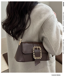 Detail of a deep brown leather baguette bag with a bold gold chain buckle on a model