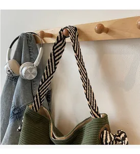 Detail of green corduroy tote with black and white striped strap on a wooden hook