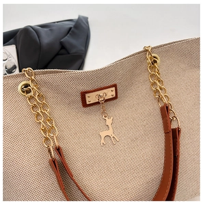 Detail of beige woven tote bag with brown leather strap and golden deer charm