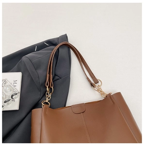 Close-up of brown leather tote bag featuring gold chain link hardware and slim handles