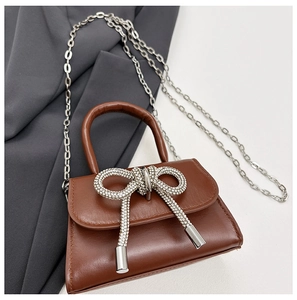 Détail d'un mini sac à main marron avec un nœud en strass brillant et chaîne argentée