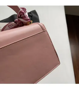 Detail of pink leather handbag showing precise stitching, gold hardware, and silk scarf wrap