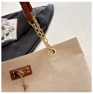 Detail of beige woven tote bag featuring gold chain strap and animal charm pendant