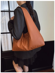 Close-up of brown leather tote bag with wide shoulder strap showing natural drape and texture