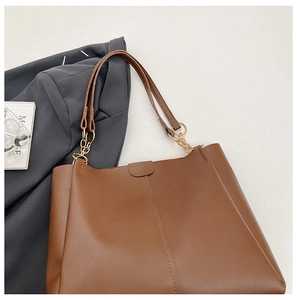 Detail of a brown leather tote bag with elegant gold chain shoulder strap on a gray suit