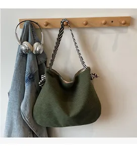 Close-up of green textured tote bag with black and white striped shoulder strap and knots