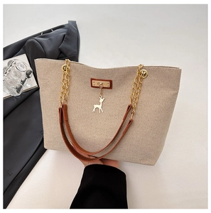 Detail of beige woven tote bag featuring a leather patch, golden deer charm, and chain strap