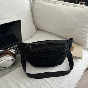 Chic black leopard print crossbody waist bag with dual zippers on a soft white sofa