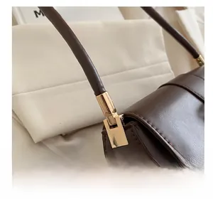 Detail of gold metal hardware connecting the handle to the dark brown leather shoulder bag