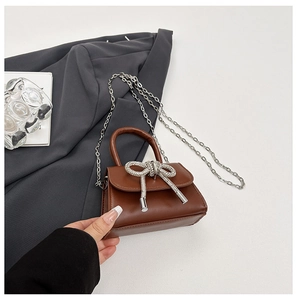 Détail d'un mini sac en cuir marron avec un grand nœud en strass et une chaîne argentée