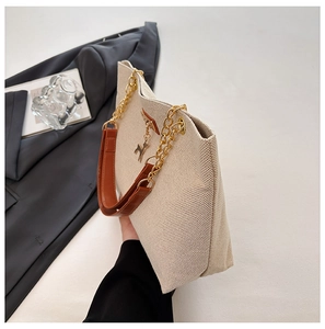 Detail of cream woven tote bag with gold chain strap and deer charm in a lifestyle setting