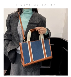 Detail of blue canvas tote bag with brown leather trim and white vertical webbing accents