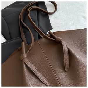 Detailed close-up of dark brown lychee pattern leather tote bag with elegant knot straps