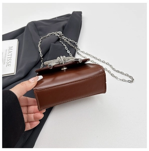 Gros plan d'un sac bandoulière marron avec boucle nœud argentée et fine chaîne
