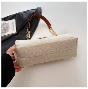 Detailed close-up of beige twill canvas texture with brown leather and gold chain strap