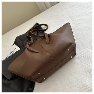 Detailed bottom view of large brown tote showing durable metal feet and lychee leather grain