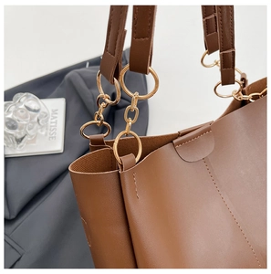 Detail of brown leather tote bag featuring gold ring chain and smooth premium texture