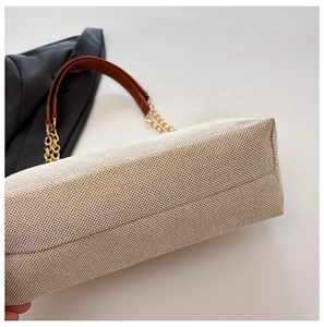 Detail of beige woven fabric tote bag with brown leather handle and gold chain strap
