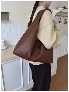 Detail shot of a dark brown large leather tote bag worn by a model in a minimalist room