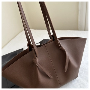Detail of a brown lychee-textured tote bag showing the knotted shoulder strap and side profile