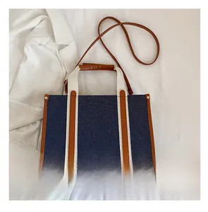 Detail of blue denim tote bag with leather trim and mobile phone for size comparison