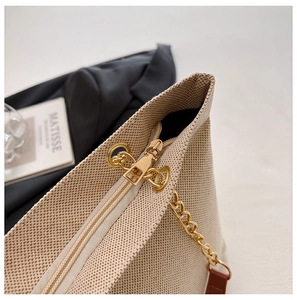 Detail of beige textured fabric bag featuring golden metal chain strap and zipper