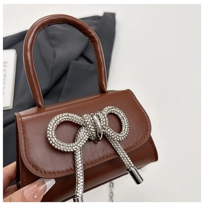 Gros plan d'un sac à main en cuir marron avec nœud en strass et bandoulière en chaîne