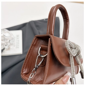 Gros plan d'un mini sac à main marron avec un grand nœud en strass et chaîne en argent