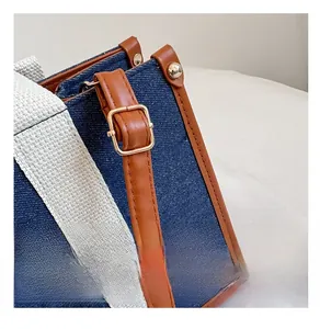 Detail of blue denim tote bag featuring brown leather trim and gold metal hardware