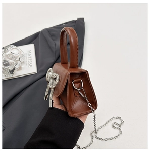 Détail d'un mini sac à main marron avec un grand nœud en strass argenté et chaîne métal