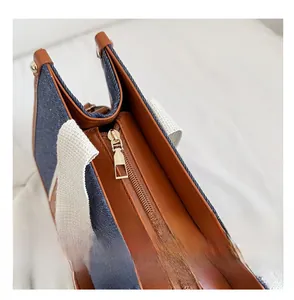 Close-up of blue denim and brown leather tote bag with a gold zipper detail