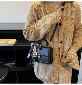 Dettaglio borsa a tracolla in pelle nera minimalista con fibbia in metallo e foulard a pois