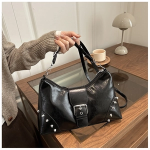 Detail of black PU leather shoulder bag with silver studs and buckles on wooden table