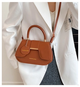 Detail of a brown saddle handbag with gold bar and adjustable strap on white blazer
