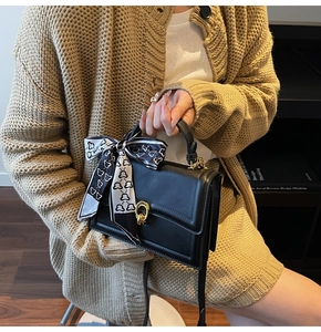 Detail der schwarzen Ledertasche mit goldenem Drehverschluss und bedrucktem Seidentuch
