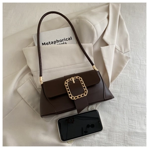Detail of dark brown leather baguette bag with gold buckle next to a phone for size