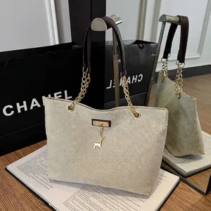 Beige woven tote bag with brown leather and gold chain handles with deer pendant