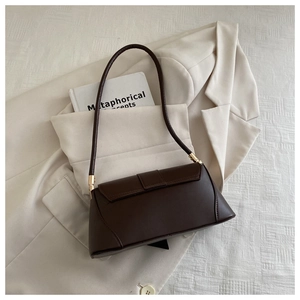 Detailed view of matte dark brown baguette bag with elegant golden hardware on beige suit