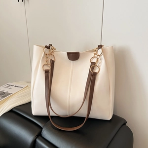 Large cream tote bag with brown handles and gold chain strap in a stylish indoor setting