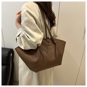 Detailed macro view of large brown pebble leather tote bag worn by model over the shoulder