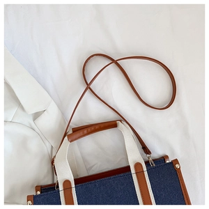 Detail of blue canvas tote bag with brown leather trim and metal rivet accents