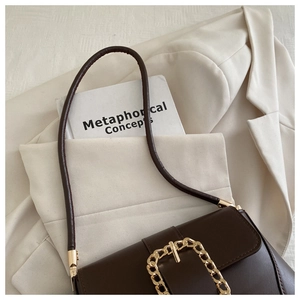 Detail of dark brown matte leather bag with golden chain buckle on white blazer