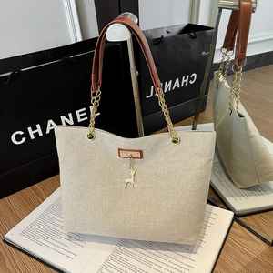 Beige canvas tote bag with brown leather straps, gold chains, and deer pendant