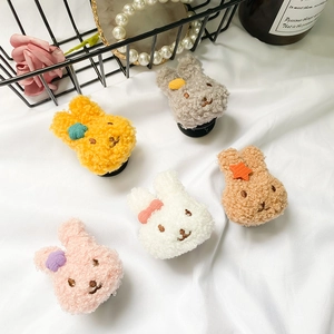 Close-up of five cute plush bunny phone grips in various colors on a white fabric background