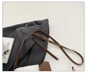 Dettaglio della tracolla in pelle marrone con fibbia dorata su borsa a secchiello bianca