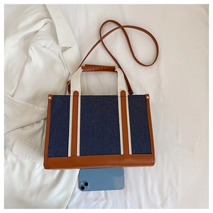 Detail view of denim tote bag with leather trim and shoulder strap on a blazer