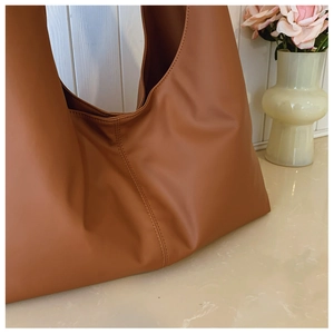 Detail of dark brown leather tote bag with vertical stitching on matte textured surface