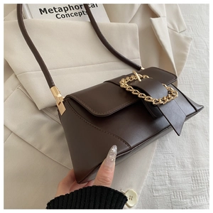 Detailed view of deep brown leather baguette bag with a bold gold chain buckle decoration